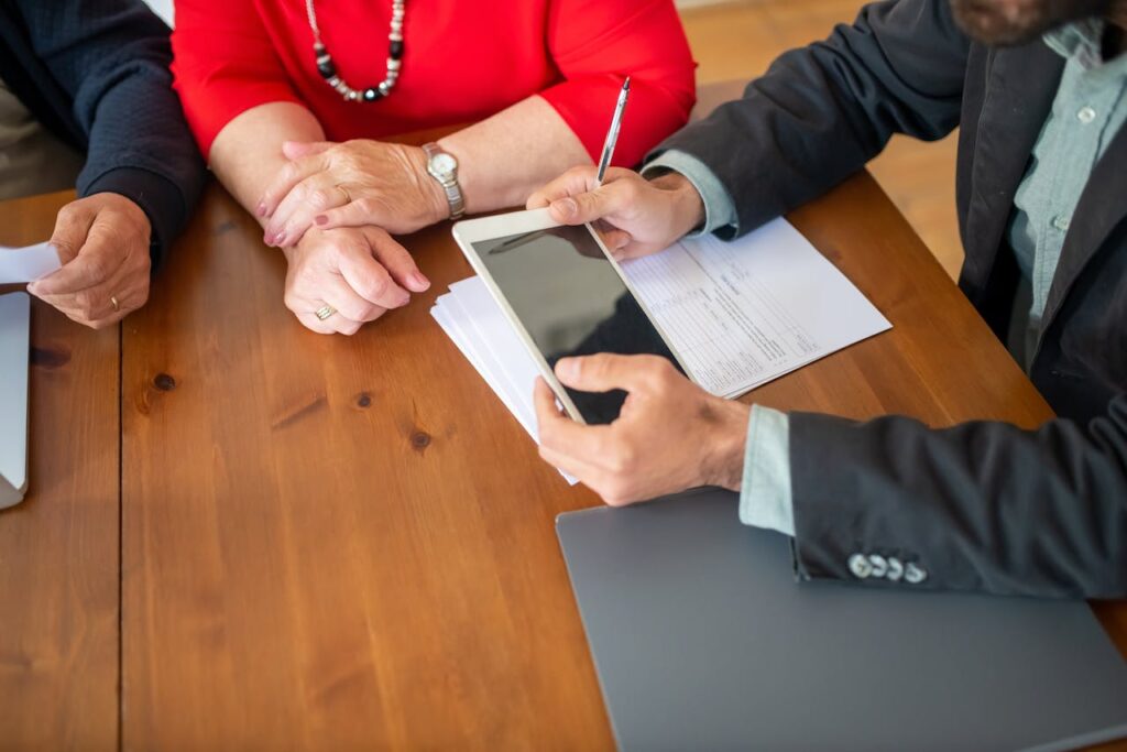 pexels-photo-8439697 Business meeting at a wooden table with consultant reviewing documents and using a digital tablet.